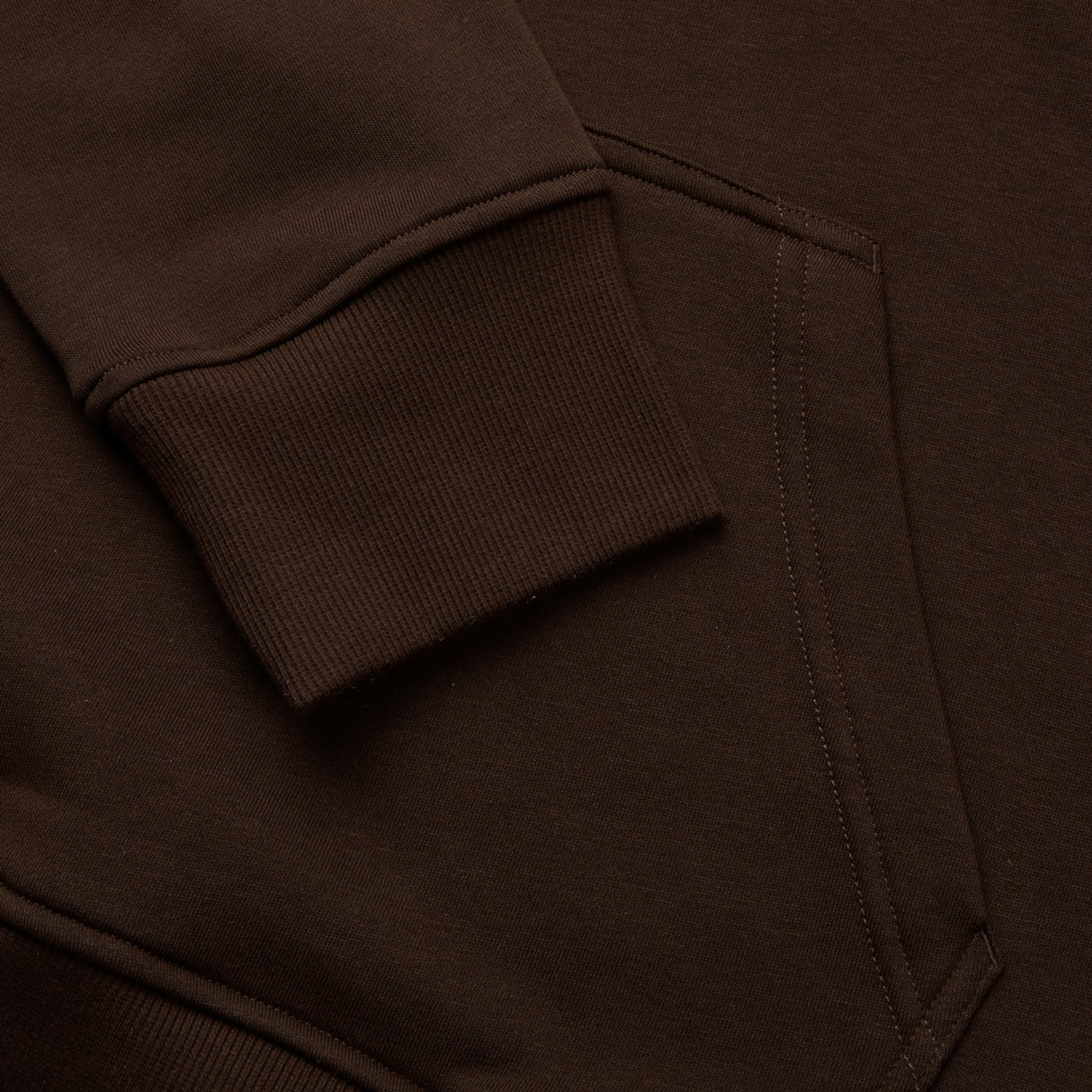 Close-up of a brown sweatshirt with ribbed cuffs and a side pocket, highlighted by bold colors reminiscent of the Canterbury Uglies Hoodie by Canterbury.