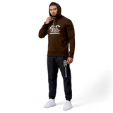 A person in a brown Canterbury Uglies Hoodie with the iconic CCC logo, paired with black sweatpants and white sneakers, stands in a neutral pose.