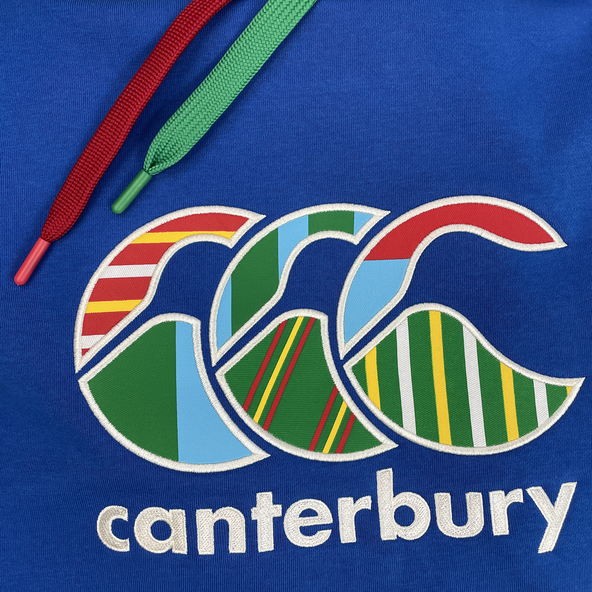 The Canterbury Uglies Hoodie boasts bold block colors, a stylized multicolored striped CCC logo, "Canterbury" branding below, and red and green drawstrings.