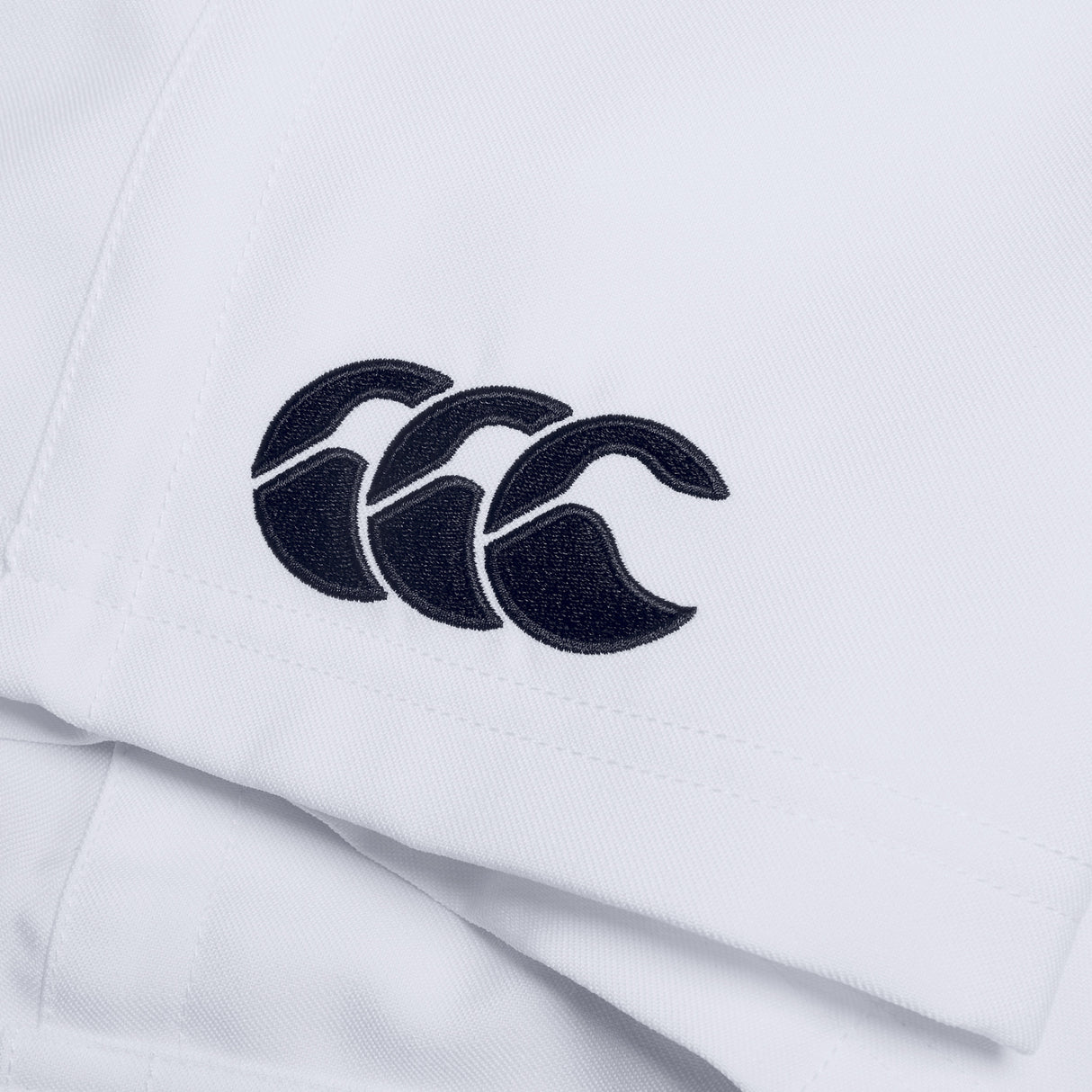 Close-up of a white fabric on the Canterbury Player's Drill Short, featuring a black embroidered logo consisting of three overlapping curves.
