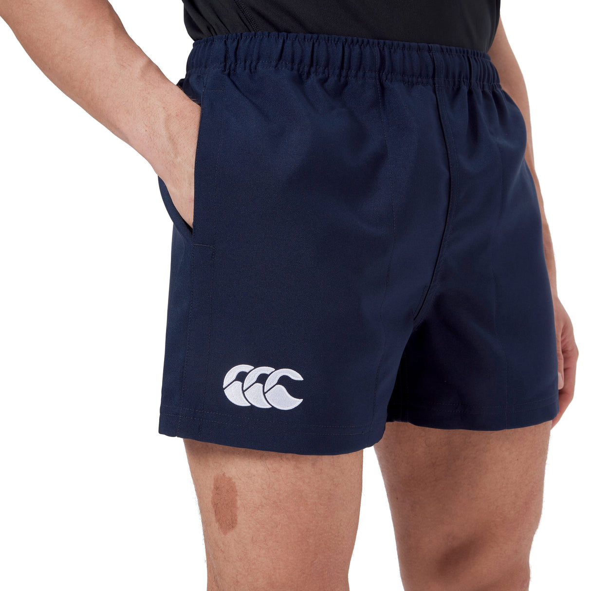 A person wearing navy blue Canterbury Player's Drill Short made from recycled fabric, featuring a logo on the left thigh, is standing with their hand in the left pocket.