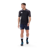 A man wearing a black Canterbury sports shirt, Canterbury Player's Drill Short, black socks, and blue shoes stands on a white background.