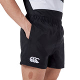 Person wearing Canterbury Player's Drill Short in black with a white Canterbury logo, standing with a hand in the pocket.