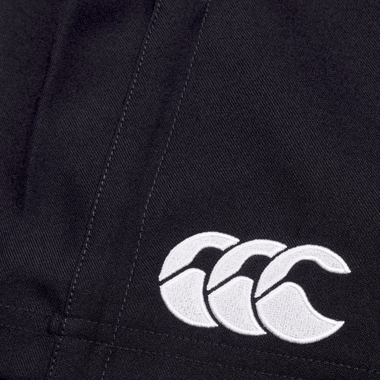 Close-up of a Canterbury Player's Drill Short in black, featuring a white embroidered logo of three interlocking crescent shapes, crafted from recycled fabric for sustainable athletic performance.