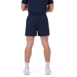 A person stands with their back to the camera, wearing a navy blue shirt and Canterbury's Professional Short 2.0, designed for durability, paired with white socks and white shoes.