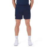 Man wears Canterbury Professional Short 2.0 in navy with adjustable fit, paired with a dark shirt, white crew socks, and white sneakers, standing hands-in-pockets against a plain background.