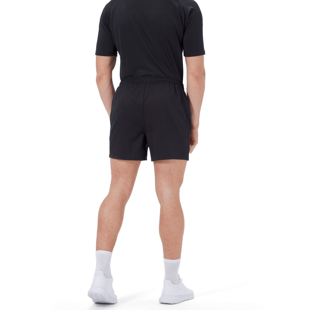 A person stands with their back to the camera, wearing a black t-shirt, Canterbury Professional Short 2.0 by Canterbury, white socks, and white sneakers against a plain white background.