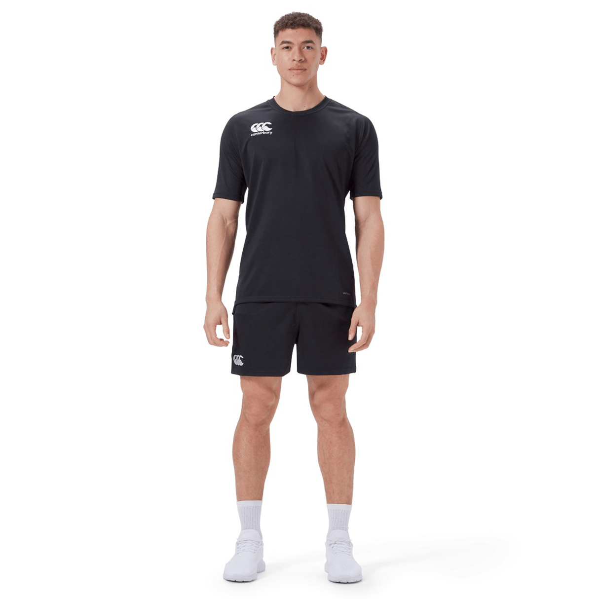 A man faces forward wearing the Canterbury Professional Short 2.0 in black, a black short-sleeve athletic shirt, white socks, and white athletic shoes against a plain white background.