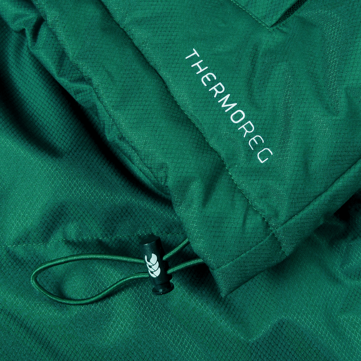 Close-up of an Ireland 24 Puffer Jacket by Canterbury in green, with the word "THERMOREG" printed on it, featuring a drawstring with a black plastic toggle.