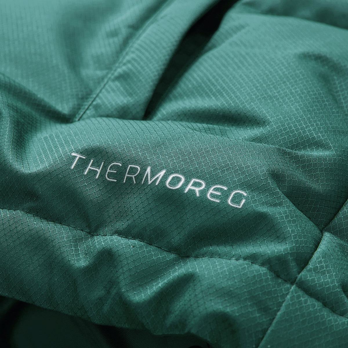 Close-up of green fabric with a subtle grid texture and the word “THERMOREG” embroidered in white thread, found on the Ireland 26 Puffer Jacket by Canterbury—a premium jacket designed for both warmth and style.