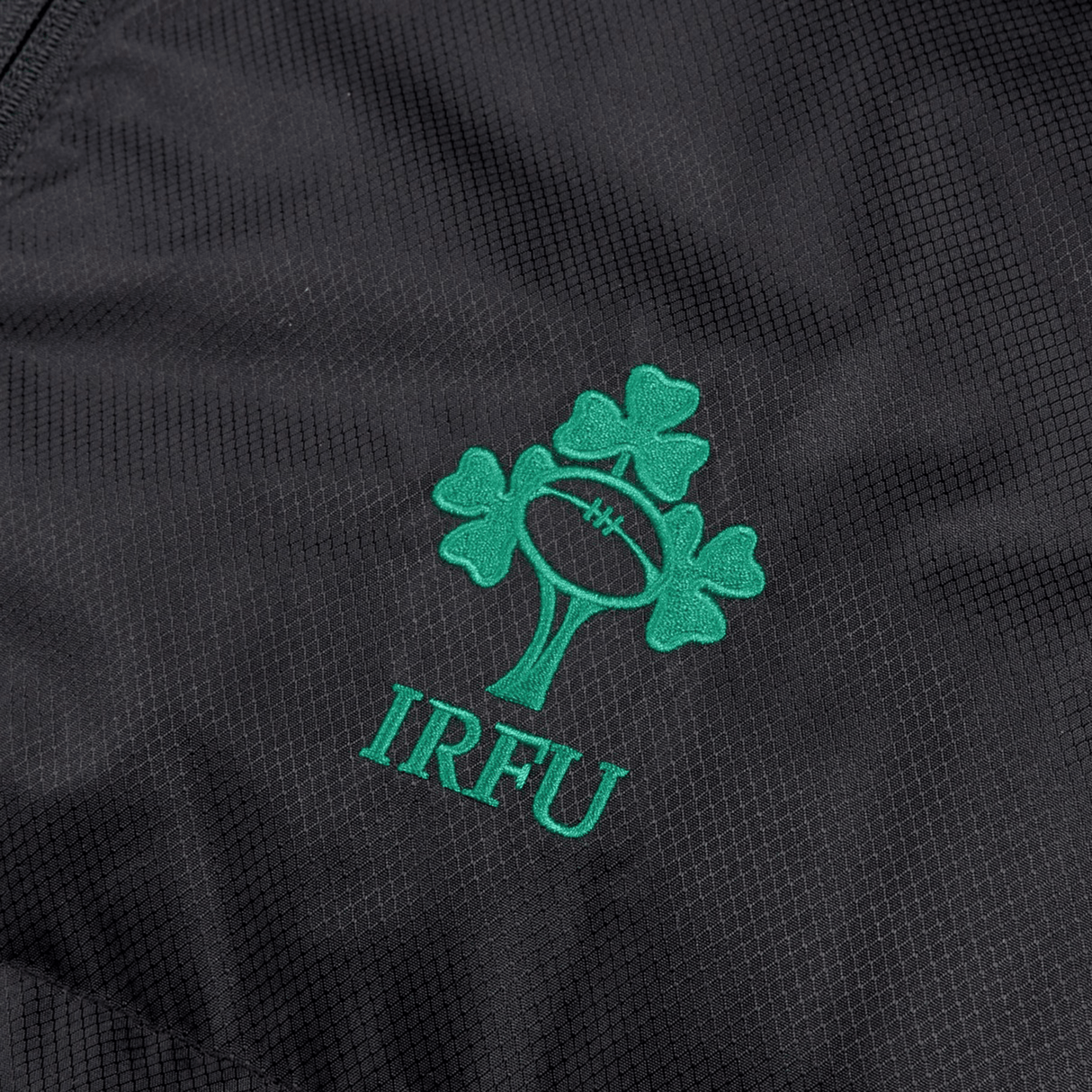 Close-up of the Ireland 24 Padded Gilet by Canterbury, showcasing a black fabric adorned with the IRFU logo, featuring a rugby ball within a tree design, embroidered in green. The material is enhanced with Vaposhield coating for added weather protection.