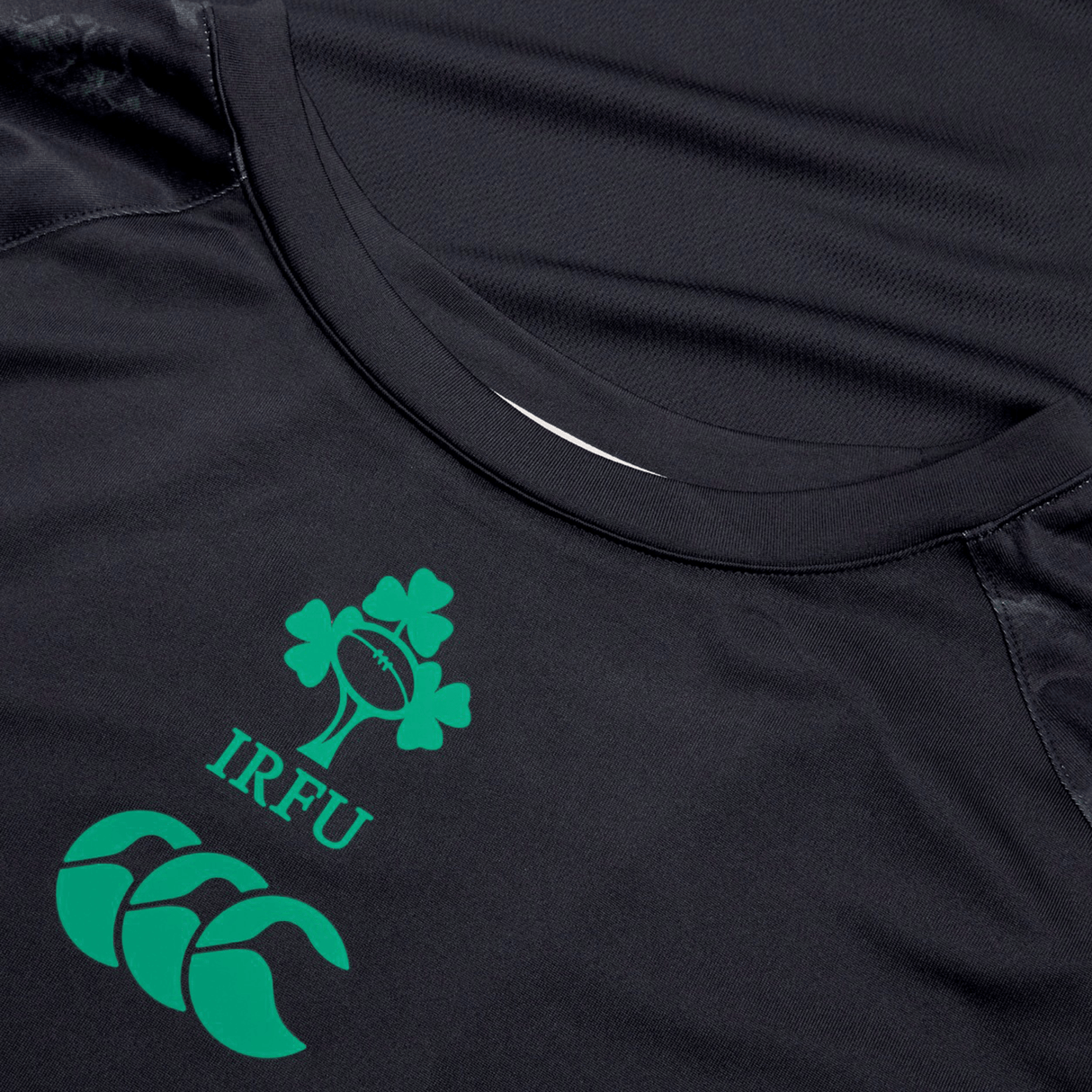 Close-up of a black sports jersey featuring the Irish Rugby Football Union (IRFU) logo and the green Canterbury logo. The Ireland 24 Superlight Training T-Shirt by Canterbury is breathable, quick-drying, and made from recycled polyester for optimal performance.