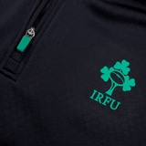 The Ireland 1/4 Zip Training Top 24 by Canterbury, featuring a dark fabric adorned with the IRFU logo—which includes a rugby ball and clover—along with a zipper that has a green pull tab, is perfect for enthusiasts.