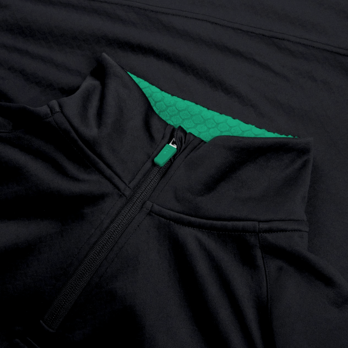 Close-up of the Ireland 1/4 Zip Training Top 24 by Canterbury, showcasing a sleek black exterior with a green inner lining and hexagonal pattern. The zipper is partially open, revealing the vibrant green interior.