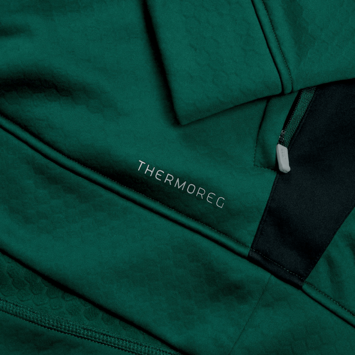 Close-up of a green Ireland 1/4 Zip Training Top 24 by Canterbury with a subtle textured pattern, featuring the word "THERMOREG" printed in silver text and a zipper pocket adorned with an Ireland 24 tag.