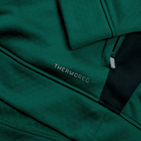 Close-up of a green Ireland 1/4 Zip Training Top 24 by Canterbury with a subtle textured pattern, featuring the word "THERMOREG" printed in silver text and a zipper pocket adorned with an Ireland 24 tag.