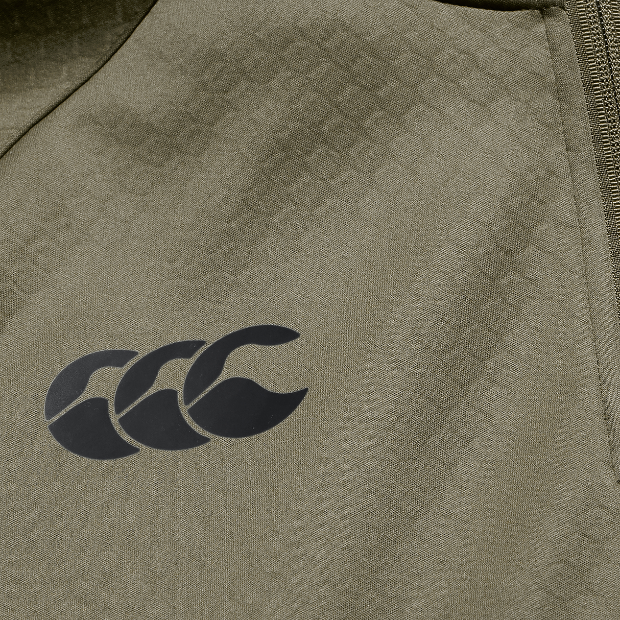 Close-up of the Ireland 25/26 Training Top by Canterbury in olive green, showcasing a black Canterbury logo and a visible right-edge zipper, crafted with advanced Thermoreg technology.