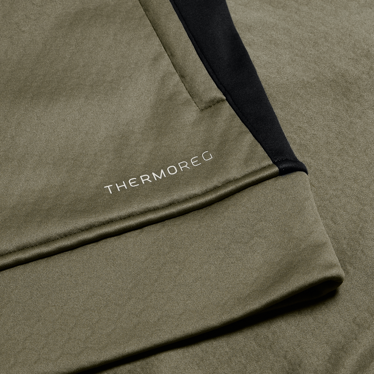 Close-up of olive green fabric with a black accent and "THERMOREG" in white, from the Ireland 25/26 Training Top by Canterbury, featuring a cozy fleece lining.