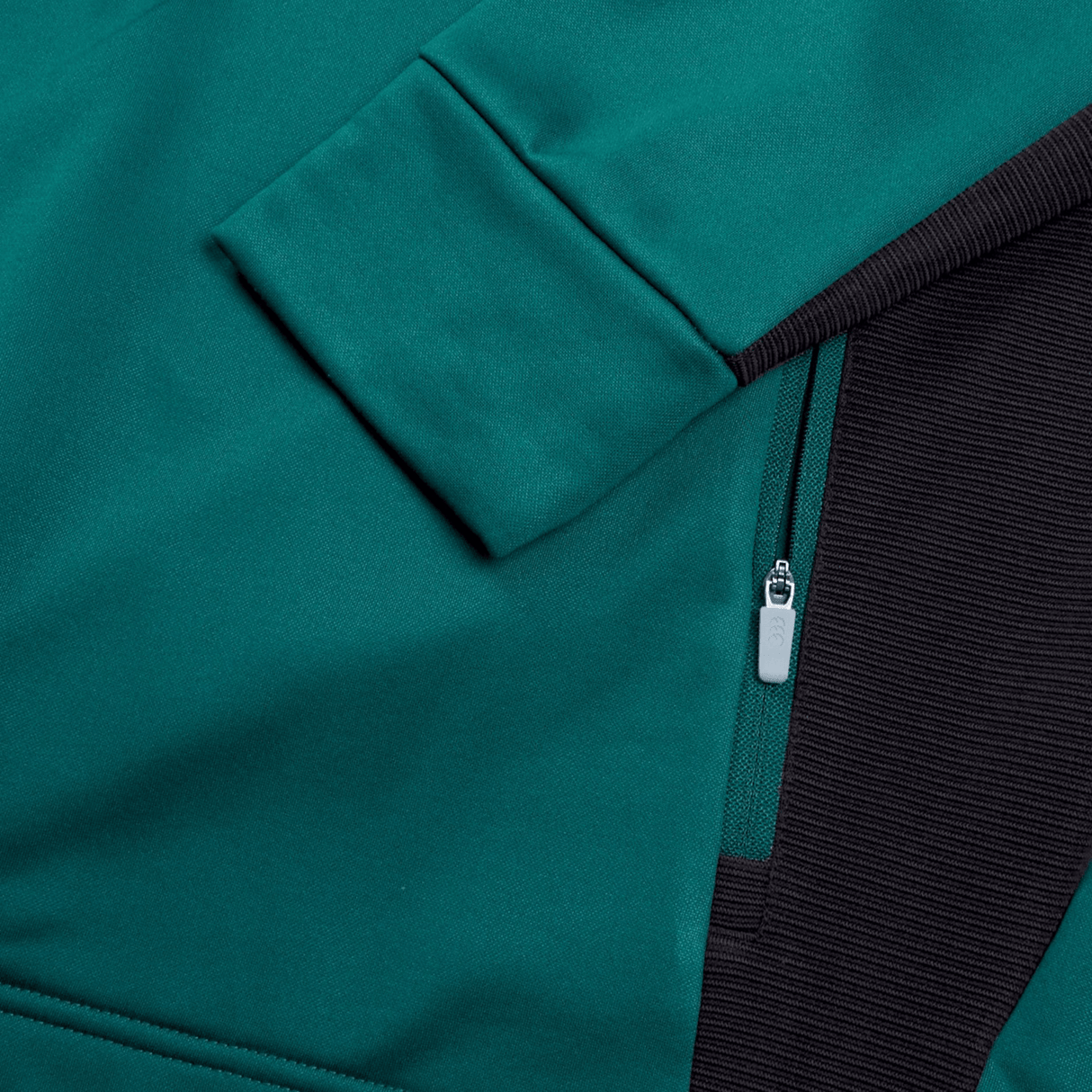 Close-up of a teal jacket showing a sleeve, zipper, and part of a black ribbed section from the Ireland Training Hoodie 24 by Canterbury made from 100% polyester.