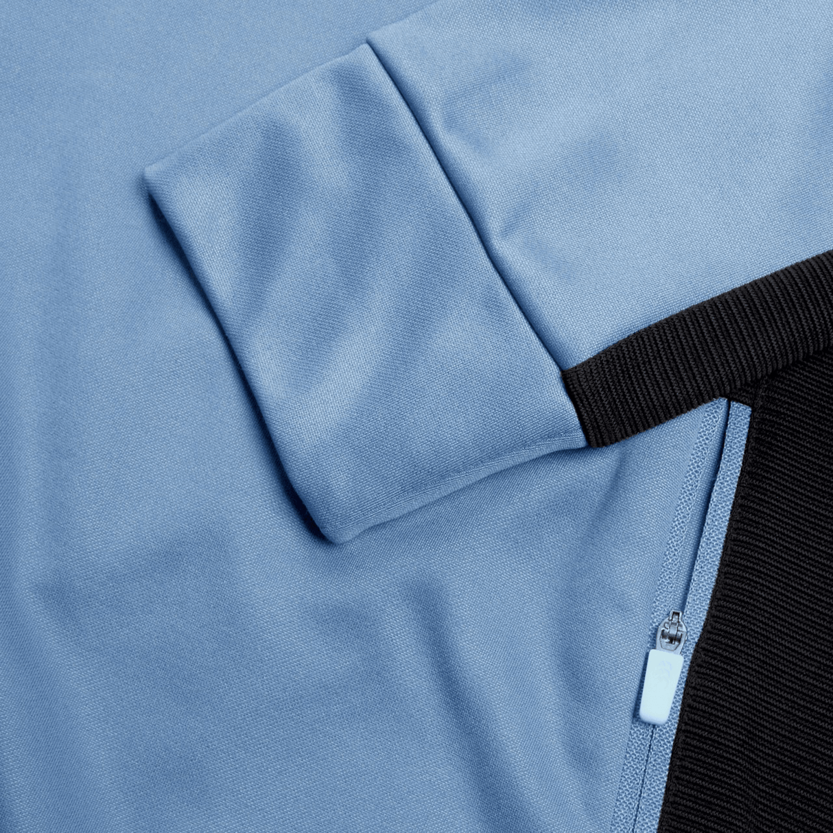 Close-up of a light blue Canterbury garment with a zippered black pocket and a folded sleeve. The polyester zipper features a light blue pull tab, adding functional style to this Ireland Training Hoodie 24 by Canterbury.