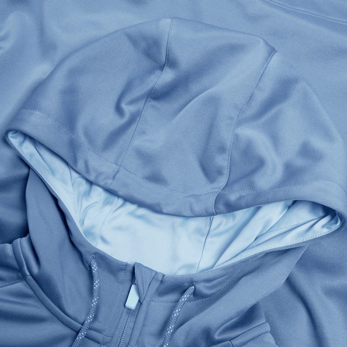A close-up of the Ireland Training Hoodie 24 by Canterbury reveals a light blue hood with part of the zipper. The polyester fabric boasts a smooth, slightly glossy finish.