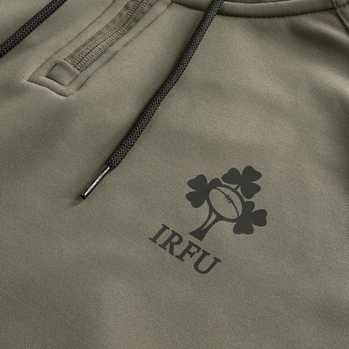 Close-up of the Ireland 25/26 Training Hoodie by Canterbury in khaki, showcasing black drawstrings and the IRFU shamrock and rugby ball logo printed on the fabric.