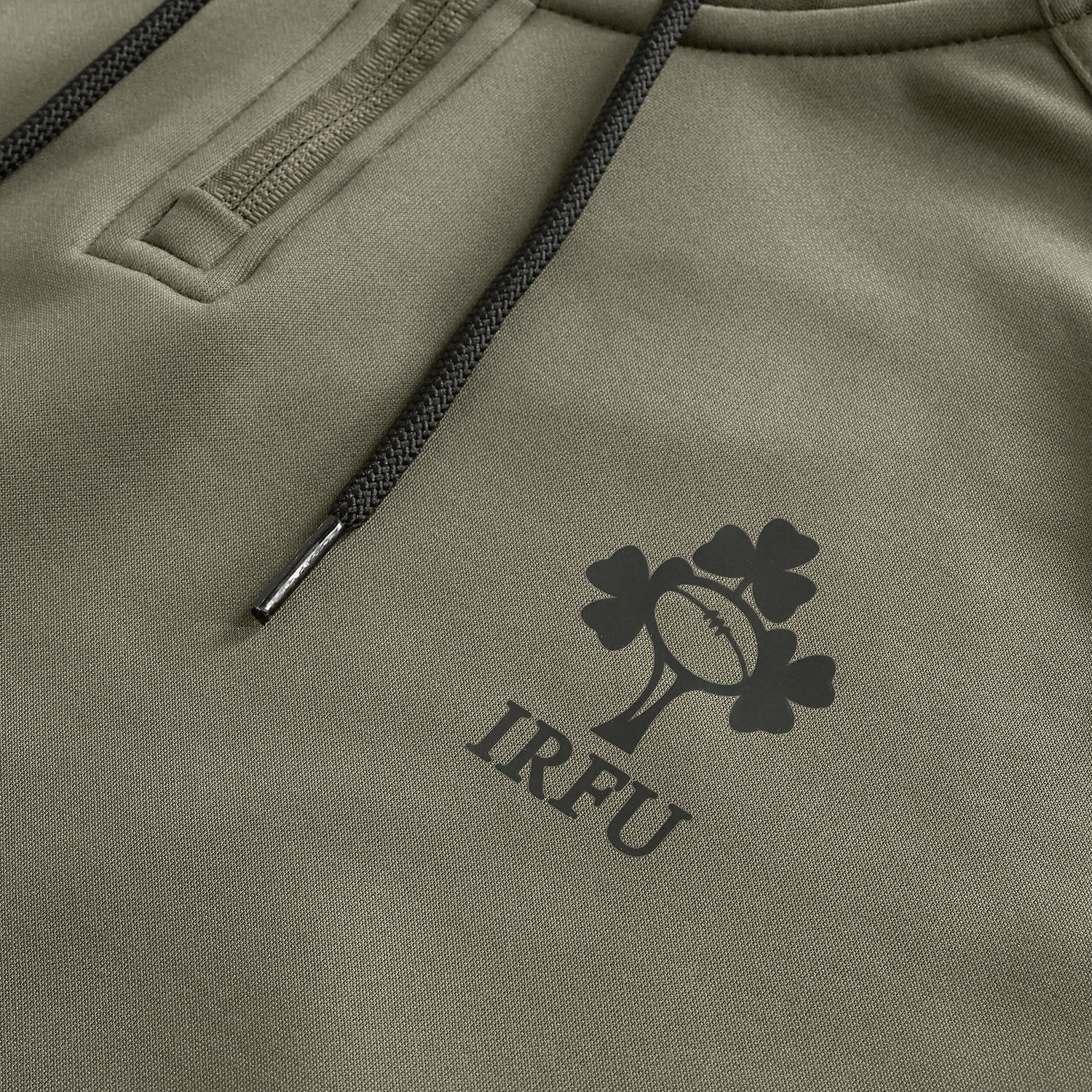 Close-up of the Ireland 25/26 Training Hoodie by Canterbury in khaki, showcasing black drawstrings and the IRFU shamrock and rugby ball logo printed on the fabric.