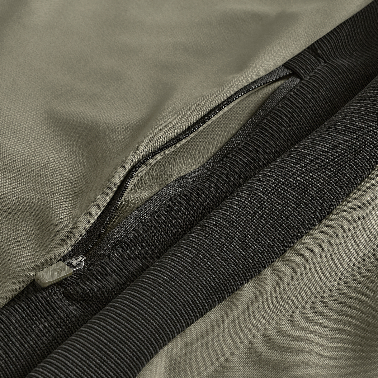 Close-up of the Ireland 25/26 Training Hoodie by Canterbury, featuring a khaki fabric, black ribbed cuff, and open zipper pocket—showcasing signature Canterbury details.