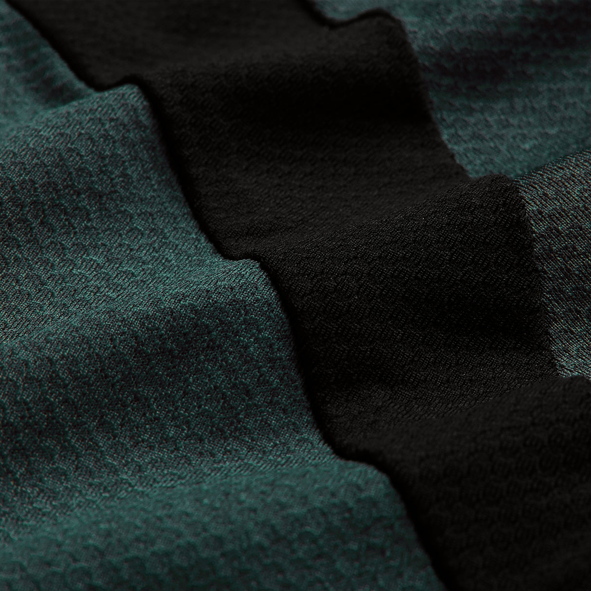 Close-up of textured fabric with alternating dark green and black wavy stripes. The surface reveals intricate knit patterns and a soft finish, showcasing Canterbury’s advanced Vapodri breathable sportswear technology found in the Ireland 26 Elite Training Tee.