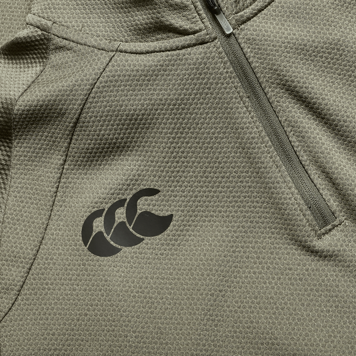 Close-up of the Ireland 25/26 Elite First Layer 1/4 Zip by Canterbury, showcasing its khaki texture, 1/4 zip pocket, and black Canterbury logo.