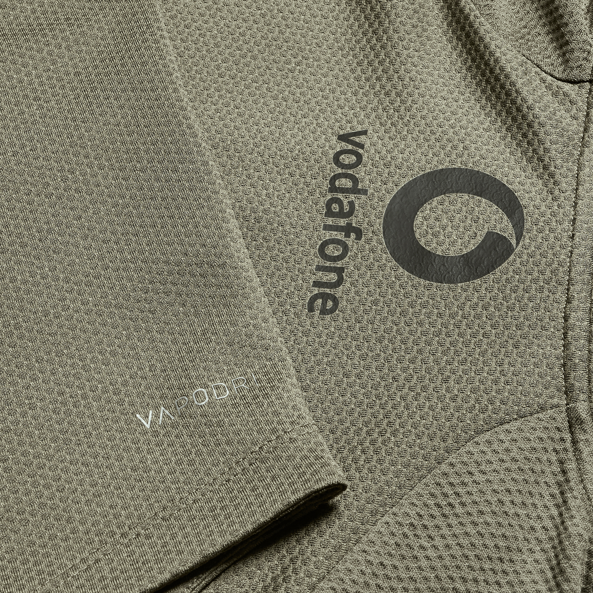 Close-up of the olive green textured fabric of the Ireland 25/26 Elite First Layer 1/4 Zip by Canterbury, with Vodafone logo and "VA MOOD" text, featuring a classic quarter-zip design.