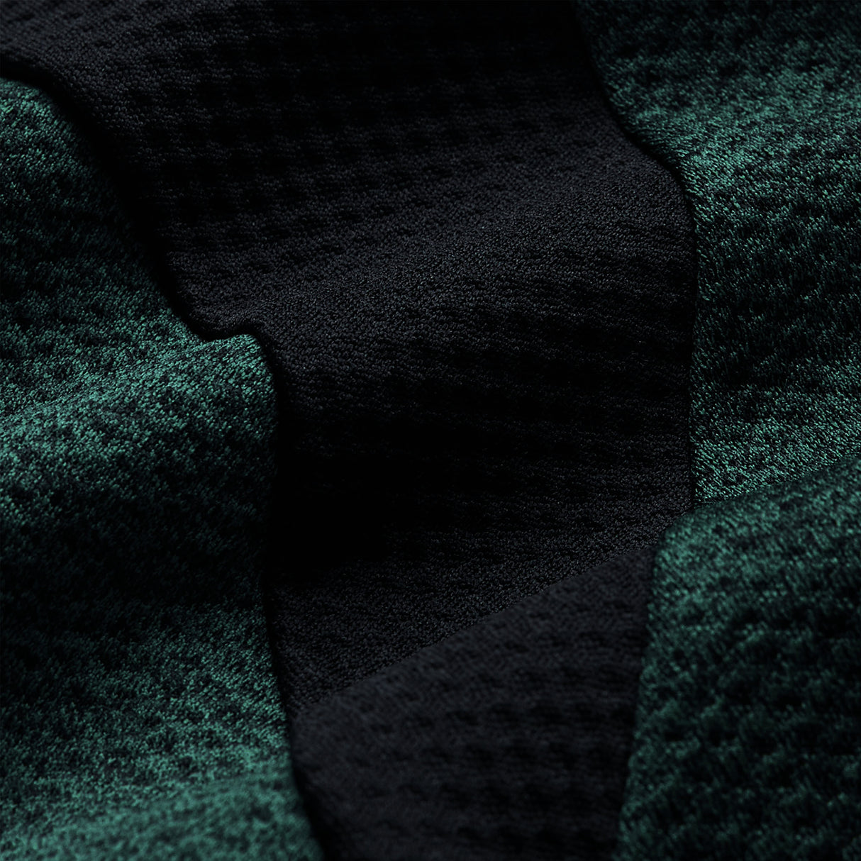 Close-up of textured dark green and black fabric with a waffle-like pattern and visible folds, highlighting the advanced Vapodri technology featured in the Ireland 26 Elite First Layer by Canterbury.