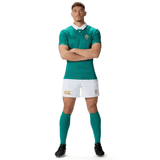 Dressed in the Canterbury Ireland 150th Anniversary Home Match Shorts and top, a man stands with arms crossed, proudly showing off his green rugby uniform complete with green socks and black shoes, all set for the home match against a pristine white background.