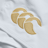 A close-up showcases the gold embroidered Canterbury logo on white fabric, featured on the Ireland 150th Anniversary Home Match Short by Canterbury.