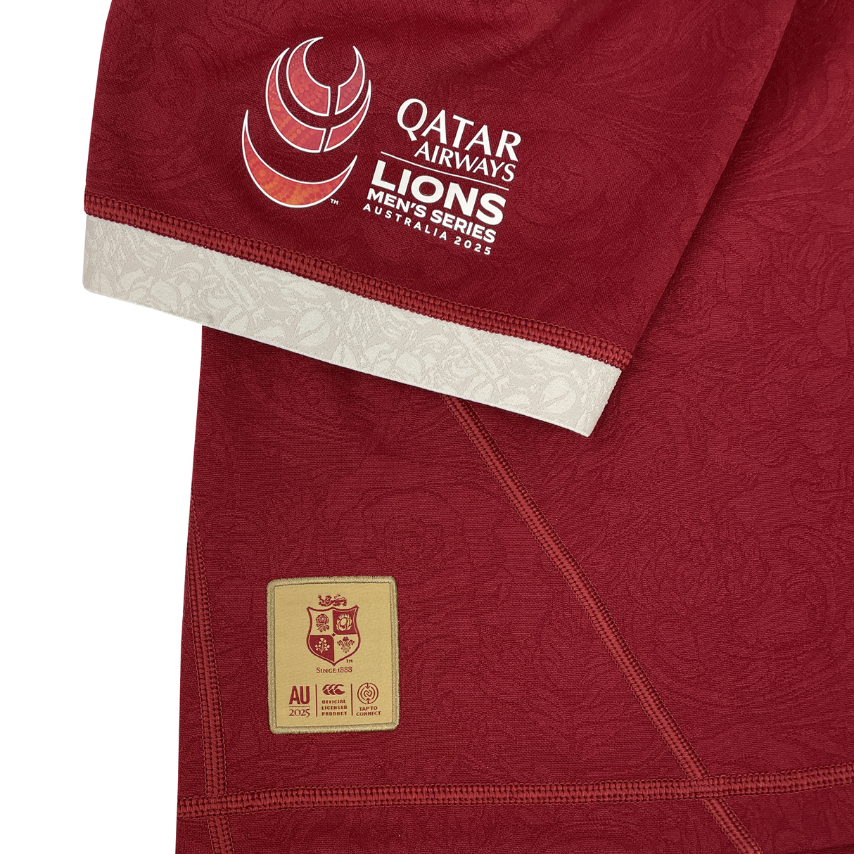 A close-up of the British & Irish Lions 2025 Players Authentic Jersey by Canterbury shows a red sports jersey featuring the Qatar Airways Lions Men's Series Australia 2025 logo on the sleeve and a lion emblem patch with text near the bottom, capturing the essence of the tour jersey.