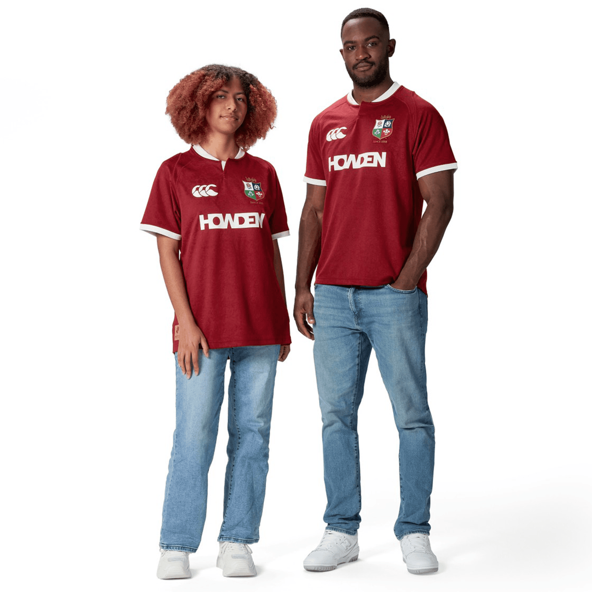 Two people wearing matching red *British & Irish Lions 2025 Players Jerseys by Canterbury* and jeans, standing against a white background. The moisture-wicking fabric of their Canterbury attire keeps them comfortable and stylish.