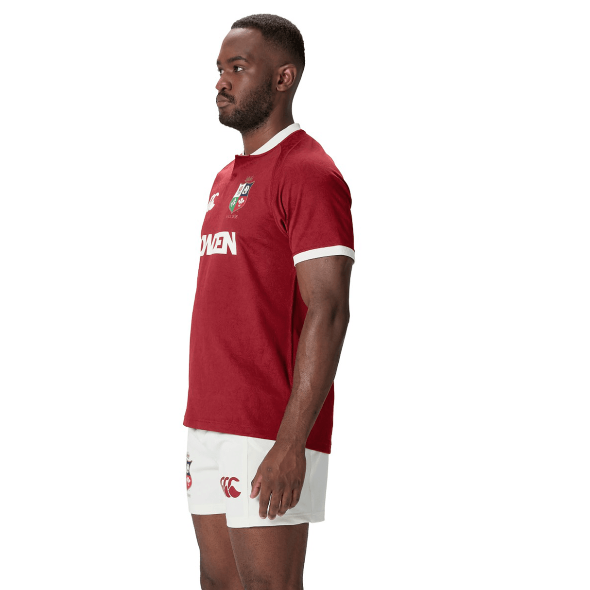 Wearing a maroon British & Irish Lions 2025 Players Jersey by Canterbury and white shorts, a person stands in profile against a white background, highlighting the garment's moisture-wicking fabric.