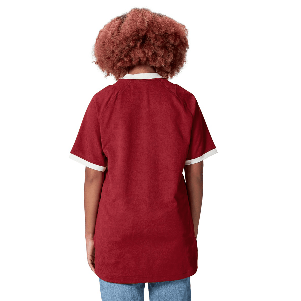 A person with curly hair, clad in a red British & Irish Lions 2025 Players Jersey by Canterbury, featuring white cuffs, is seen from behind.