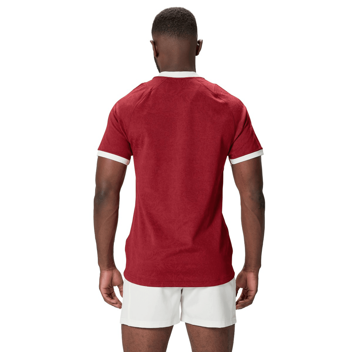 A person in a red shirt and white shorts, akin to the British & Irish Lions 2025 Players Jersey by Canterbury, stands with their back to the camera against a plain white background.