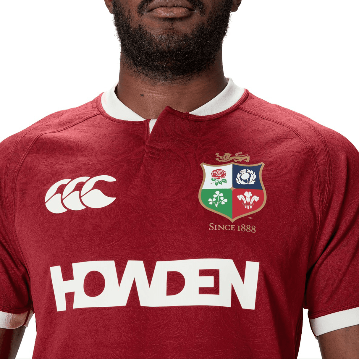 A person wearing the British & Irish Lions 2025 Players Jersey by Canterbury in red, featuring team logos and "HOWDEN" on the front, crafted from moisture-wicking fabric.
