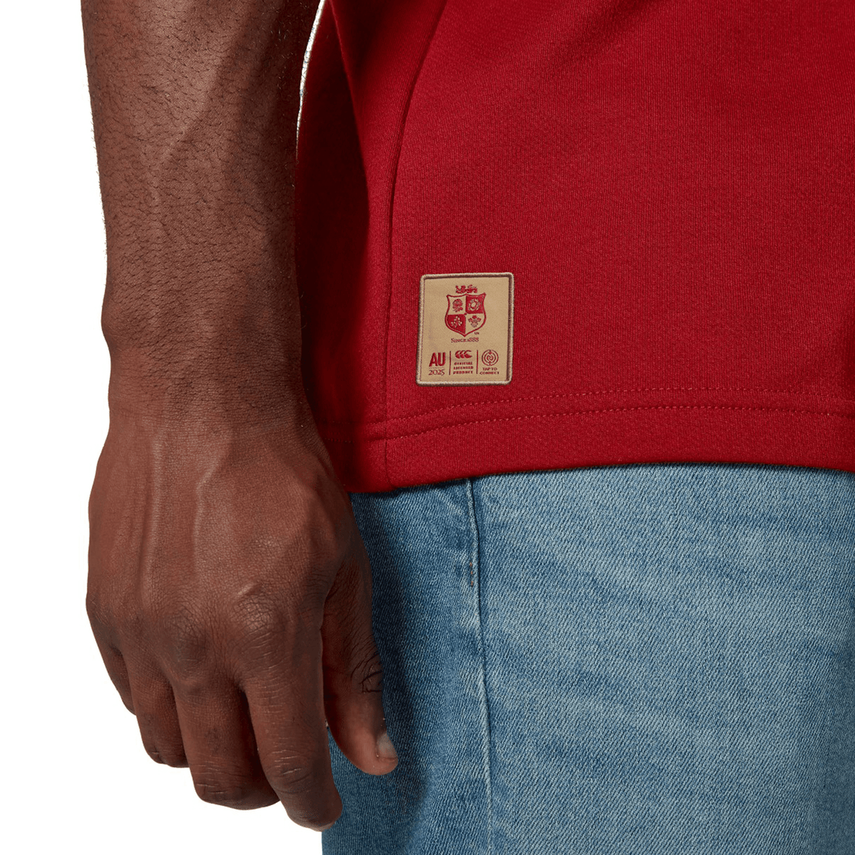 A person in a vibrant British & Irish Lions 2025 Classic Jersey by Canterbury and blue jeans is shown from the waist down, standing with their right arm by their side.