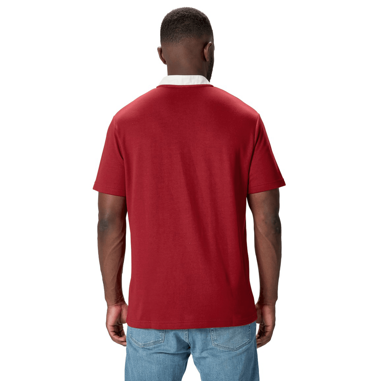 A person sporting the British & Irish Lions 2025 Classic Jersey by Canterbury, featuring a Red Dahlia color with a white collar, stands facing away, paired with blue jeans.