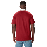 A person sporting the British & Irish Lions 2025 Classic Jersey by Canterbury, featuring a Red Dahlia color with a white collar, stands facing away, paired with blue jeans.