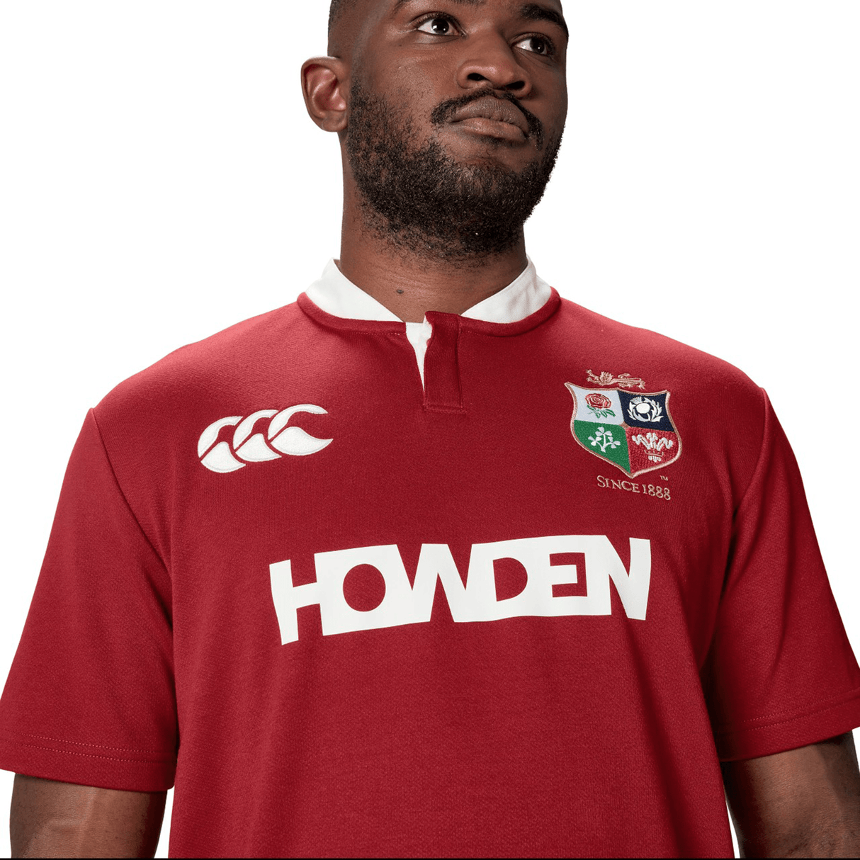 A person is wearing the British & Irish Lions 2025 Classic Jersey by Canterbury in red, featuring logos such as "Howden" and "Canterbury," as well as a "Since 1888" emblem.