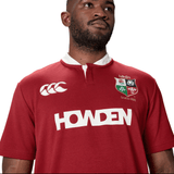 A person is wearing the British & Irish Lions 2025 Classic Jersey by Canterbury in red, featuring logos such as "Howden" and "Canterbury," as well as a "Since 1888" emblem.