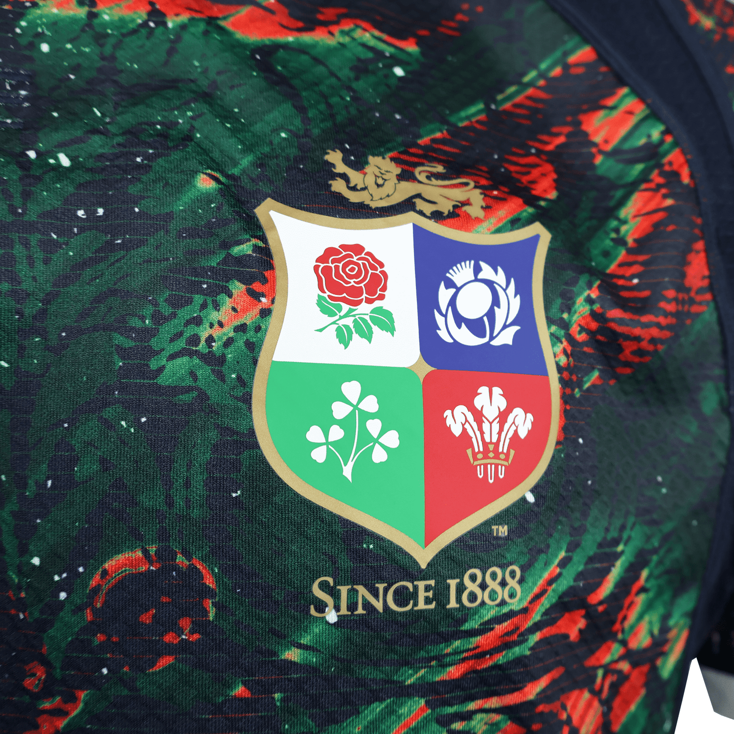 The British & Irish Lions 2025 Replica Warm Up Jersey by Canterbury features an athletic fit with a multicolored crest displaying four symbols and "Since 1888" on a dark, patterned background made from moisture-wicking fabric.