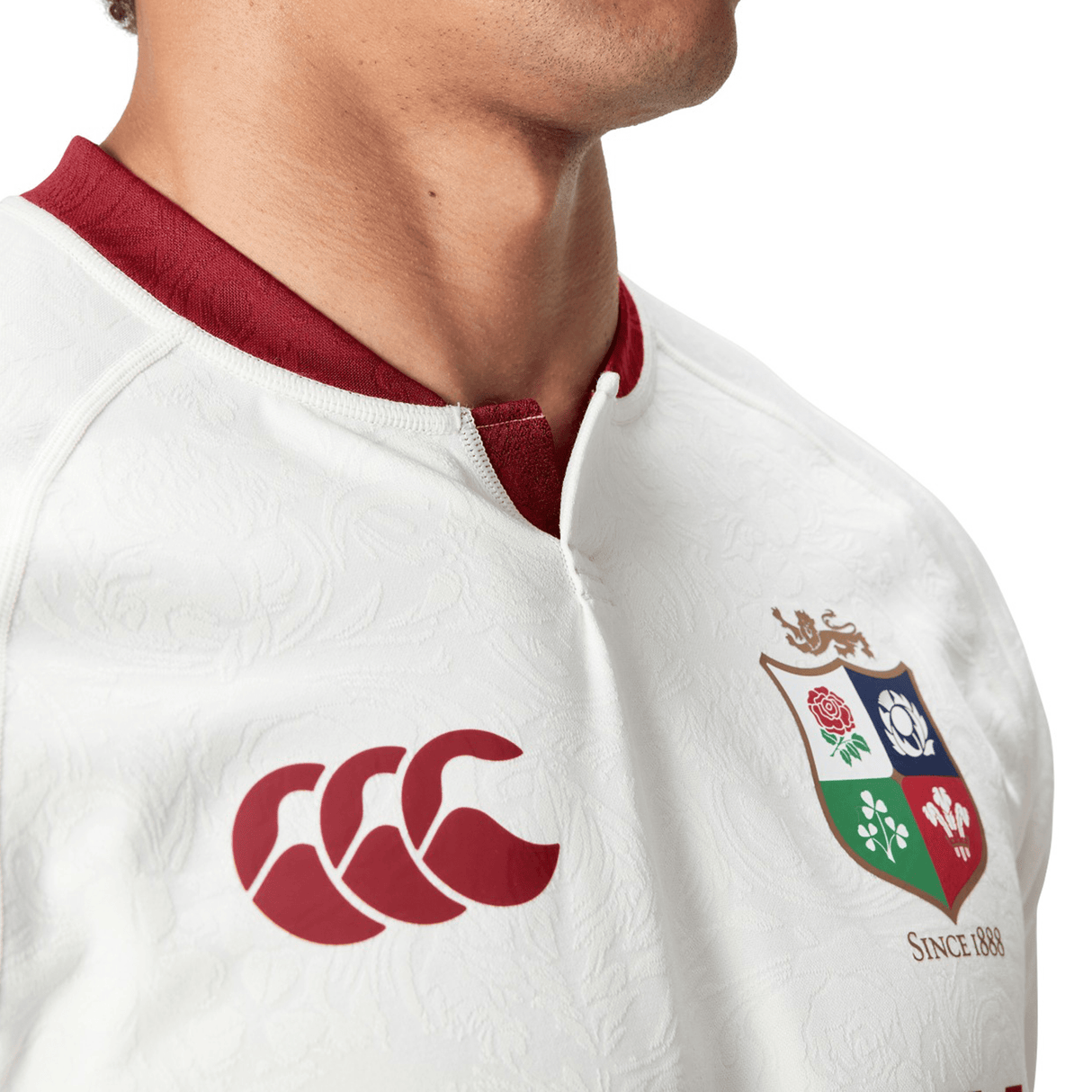 Close-up of a person wearing the British & Irish Lions 2025 Training Jersey by Canterbury in white with red details, highlighting ergonomically positioned panels for added comfort. The jersey prominently displays the Canterbury logo along with the British & Irish Lions emblem, reflecting the design of the official replica training jersey.