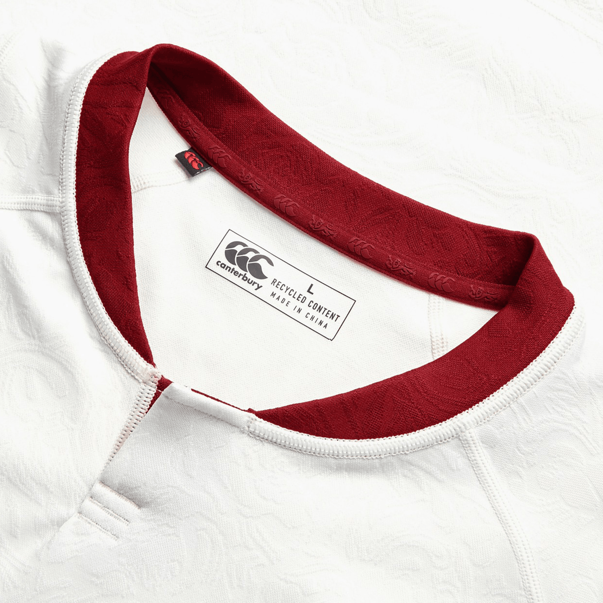 Here is a close-up of the British & Irish Lions 2025 Training Jersey by Canterbury, featuring a striking red collar against its white fabric. The jersey is labeled as size L and boasts recycled content, with ergonomically placed panels designed for enhanced comfort and performance.