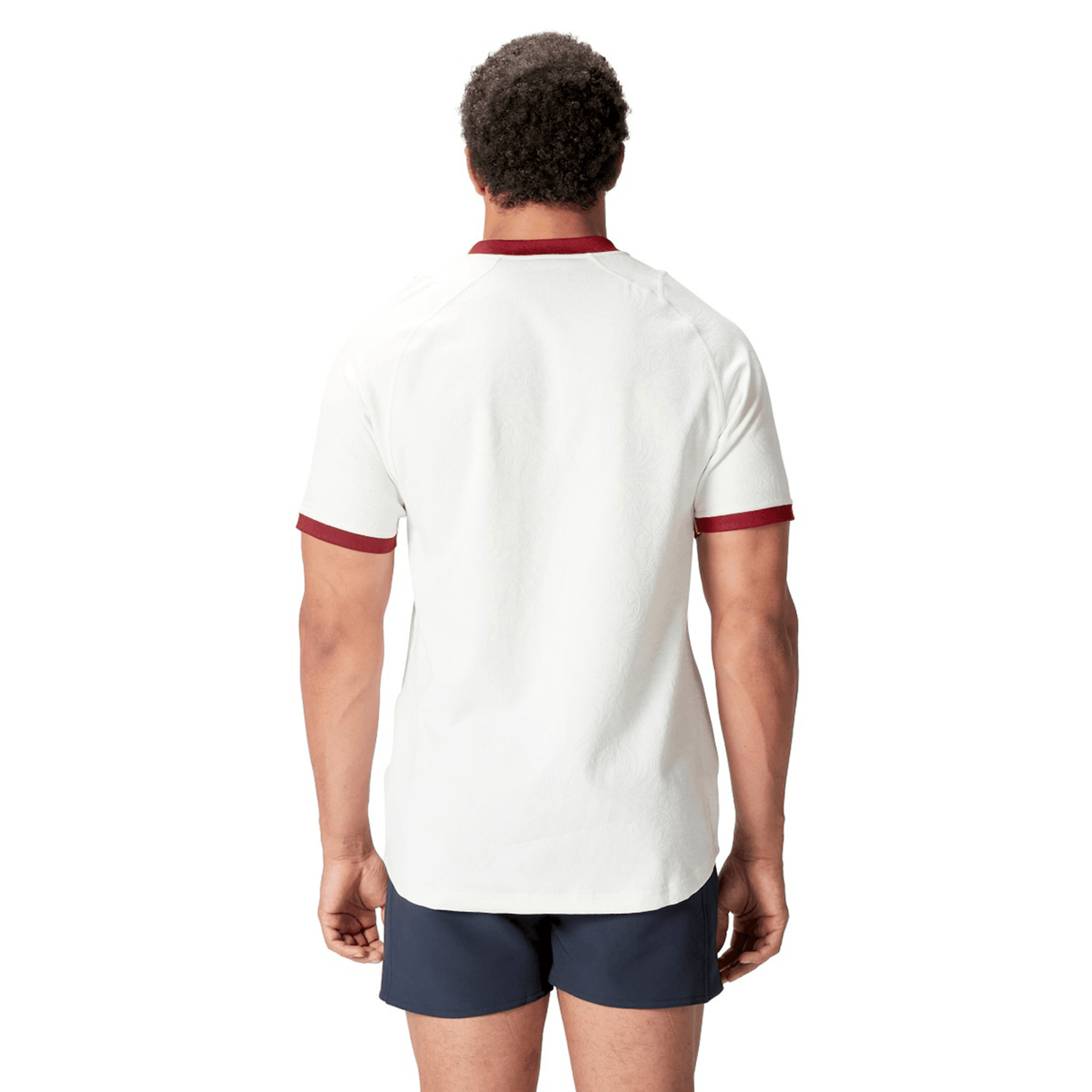 A person wearing the British & Irish Lions 2025 Training Jersey by Canterbury, featuring a white design with red trim, along with dark shorts, stands with their back to the camera.