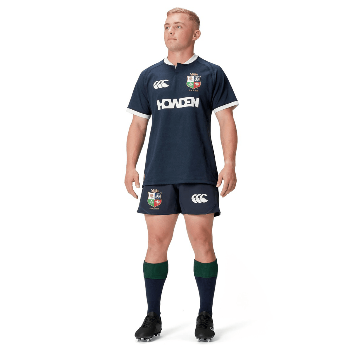 A person in the British & Irish Lions 2025 Training Jersey by Canterbury, a navy rugby uniform with logo, stands with hands at sides, looking upward. This attire from Canterbury is inspired by the classic style of the British & Irish Lions and features ergonomically placed panels for enhanced movement and comfort during play.